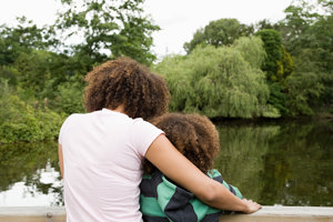 Mother with arm around her son on a park bench, looking at a lake together, the mother reflecting on a whole lifetime with migraine