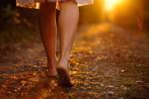 Shot of woman's legs walking towards a brighter part of the woods symbolizing her turning a corner with migraine