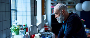 Stressed caregiver looks out of window as he considers all that lies ahead for him that day with his loved one and daughter