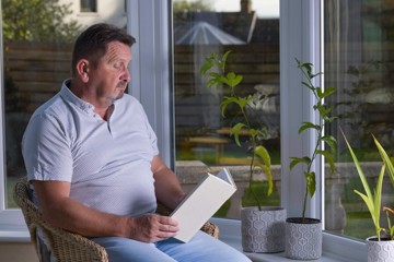 A man sits at a table with a book and a plant, reflecting on strategies for mental reset amid heart failure challenges.