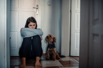 Woman hunched down on floor with her dog struggling with mental health stigma