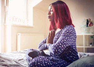 Woman meditating on her bed, gathering strength to face future migraine struggles