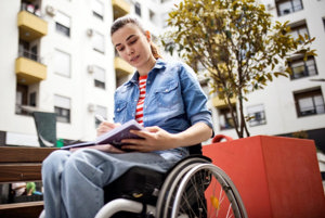 Woman sitting in wheelchair outside writing therapeutic poetry about migraine