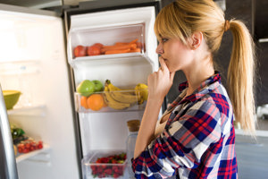 Woman staring thoughtfully into her fridge, unsure about her appetite