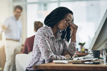 Woman suffering from migraine symptoms as coworkers talk about her behind her back