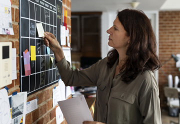 Woman with ADHD using a wall chart calendar and sticky notes to track daily tasks