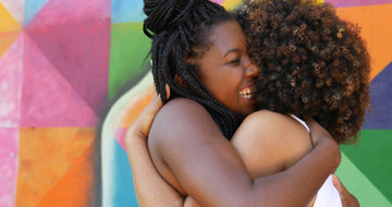 Women hugging in front of a colorful wall