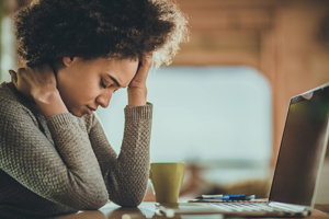 Young black woman struggling with migraine takes a work break to try and relieve her pain.