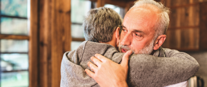 An older man embraces his son warmly in a cozy kitchen, showcasing a moment of love and connection between them.