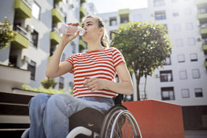 A woman in wheelchair drinking water to avoid triggering migraines