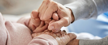 A caregiver gently holds the hand of an elderly individual, symbolizing compassion and shared wisdom in caregiving.