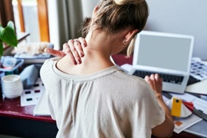 Woman at desk massages her neck to ease her pain and tension