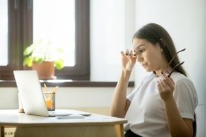 Woman working at laptop, struggling with migraine-triggering eyestrain when not wearing her glasses