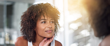 A woman gazes into a mirror, reflecting on her face, embodying strength through affirmations during tough days.