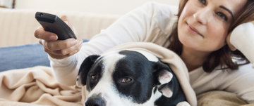 A woman relaxes on a couch with a dog, illustrating the calming effect pets can have on stress and anxiety.