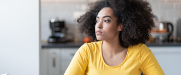 A woman with an afro sits at a table, reflecting on her journey to overcome depression and isolation.